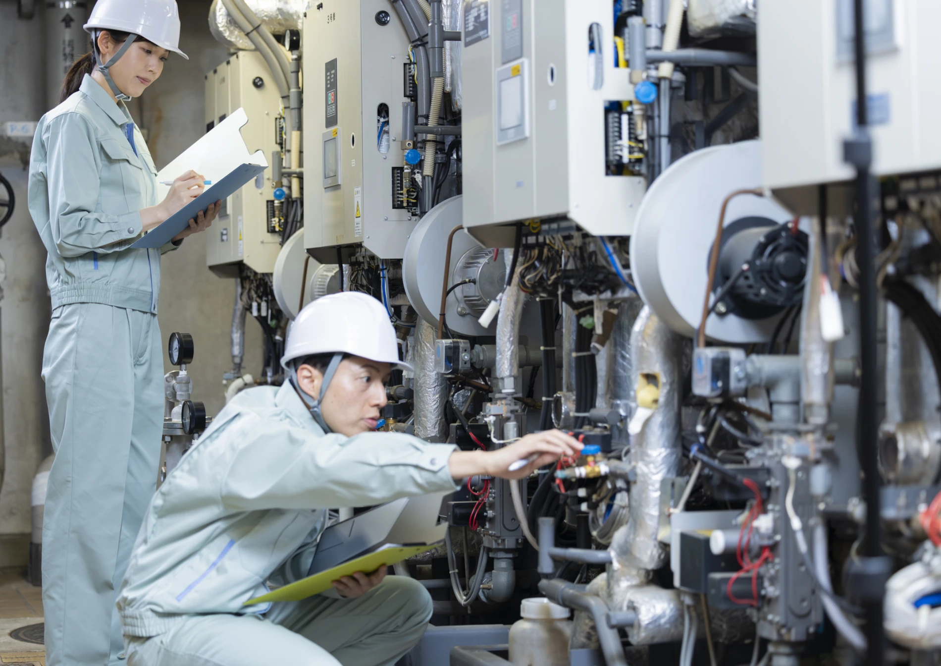 設備点検を行う2人の作業員。1人がチェックリストを記入し、もう1人が機械を確認している様子