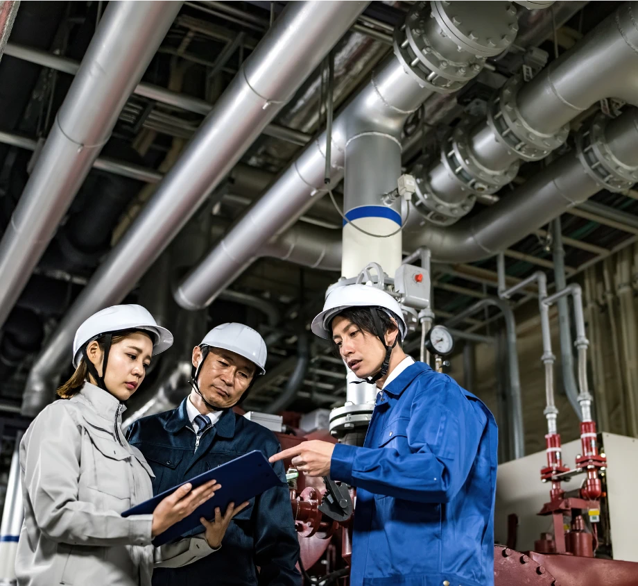 工場内で配管設備を前に打ち合わせをする3人の技術者