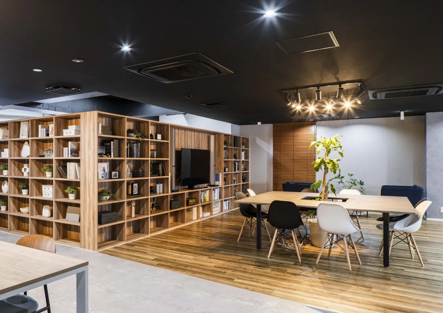 木目調の書棚と大きなテーブルがあるモダンで開放的なオフィス休憩スペース