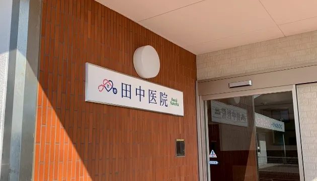 田中医院の看板。ピンクと青の聴診器と家のロゴマークが特徴