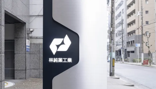 林純薬工業の自立型看板。白く光るロゴと社名が都会の街並みに映える