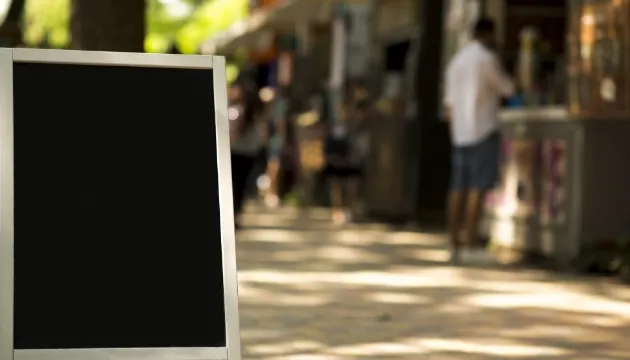 通りに置かれた黒いスタンド看板（A型看板）。背景には歩行者がぼやけて写っている