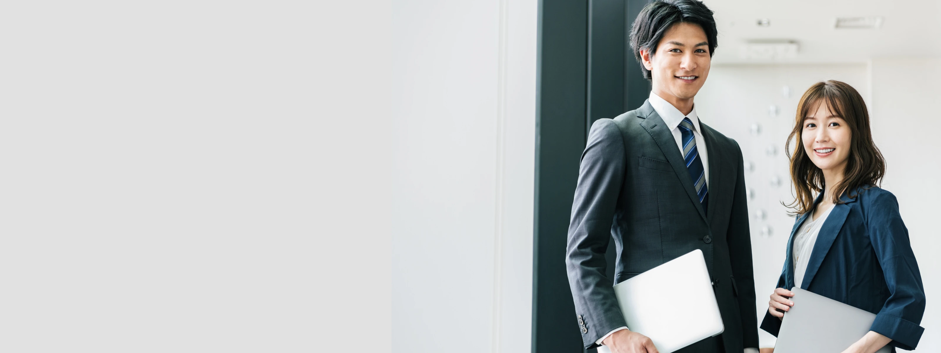 ノートパソコンを持ち、笑顔でこちらを見つめる若手ビジネスマンとビジネスウーマンの男女