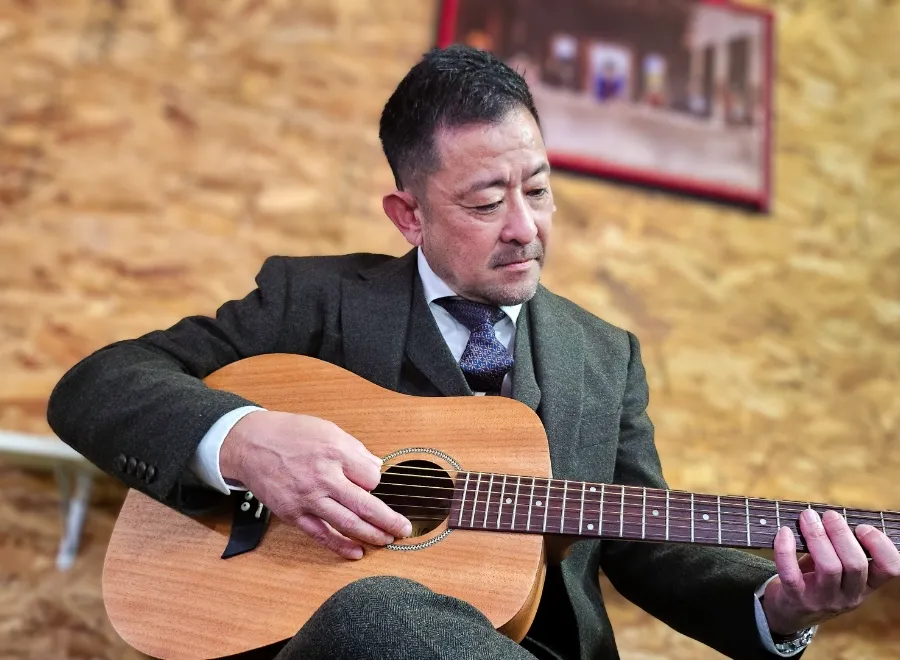 室内でアコースティックギターを弾くスーツ姿の男性