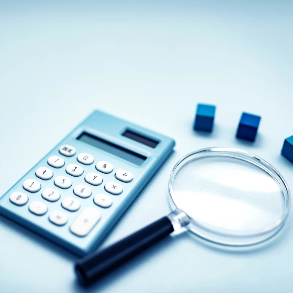 電卓と拡大鏡、青い積み木が置かれたデスク。緻密な計算や調査をイメージ