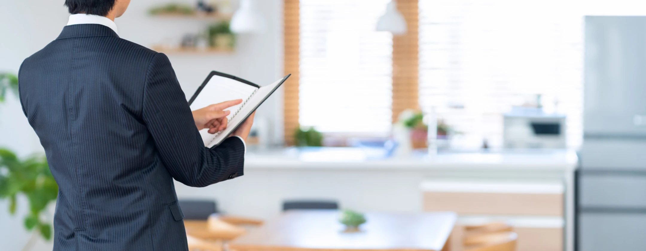 明るいリビングで手帳を確認するスーツ姿の男性の背中