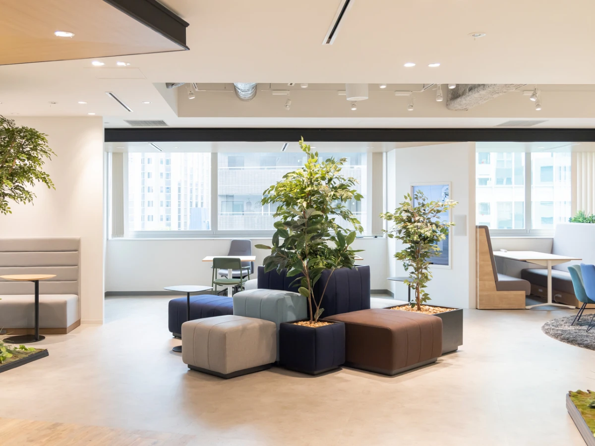 観葉植物とカラフルなスツールが配置された、開放的でモダンなオフィスのリフレッシュスペース