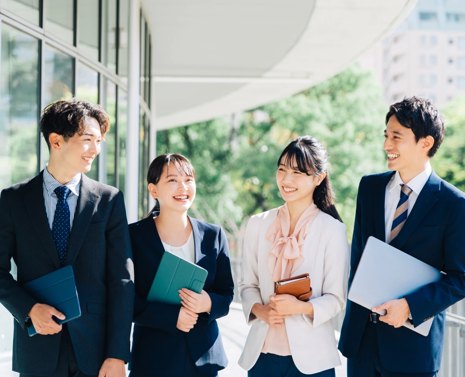 笑顔で談笑しながら屋外を歩くスーツ姿の若手ビジネスパーソン男女4人