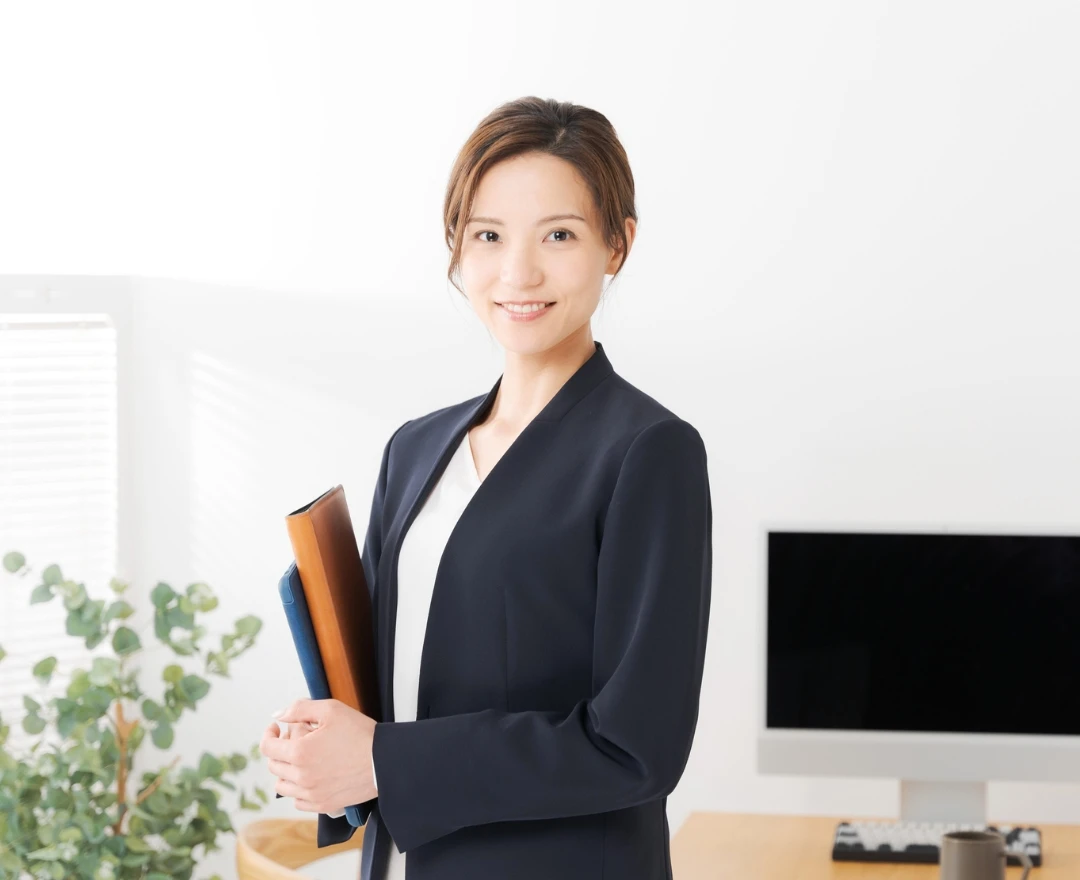 オフィスでファイルを持ち、カメラに向かって微笑むスーツ姿の女性社員