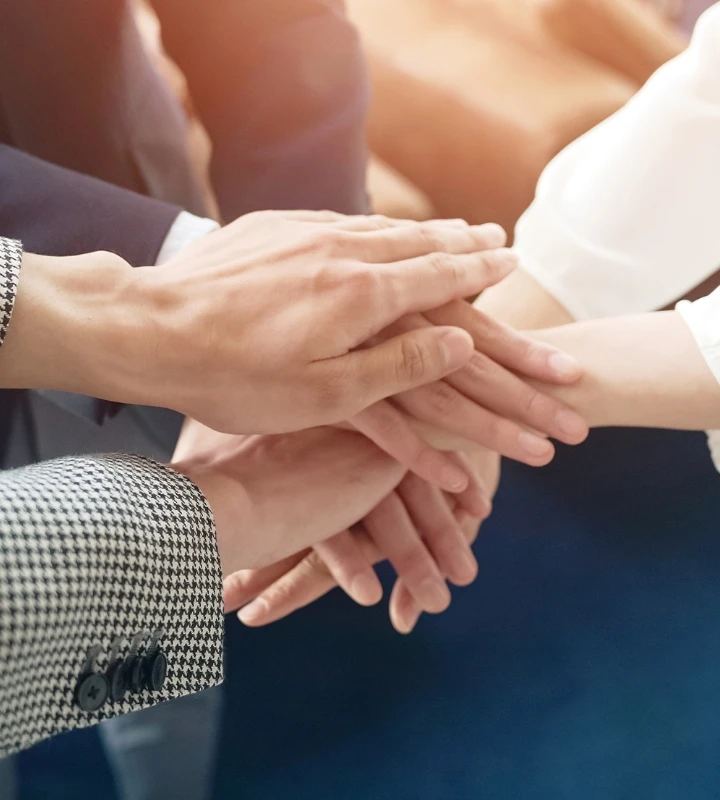 チームワークを象徴する、円になって手を重ね合わせるビジネスパーソンたちの手元