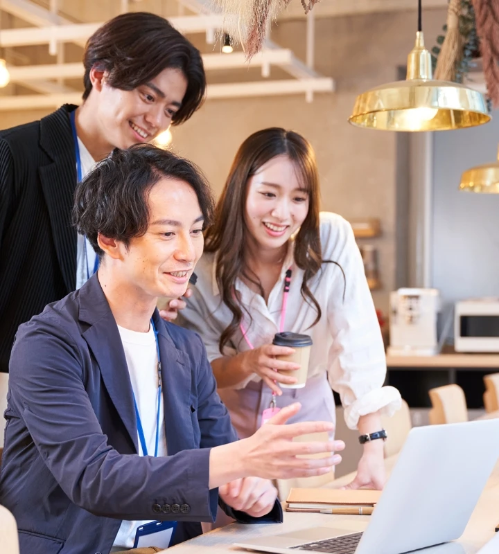 カフェのようなカジュアルな空間でパソコン画面を見ながら相談する男女3人の社員