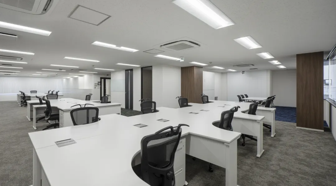 白を基調とした広々としたオフィスエリア。整然と並ぶ白いデスクと黒のオフィスチェア、清潔感のある明るい照明