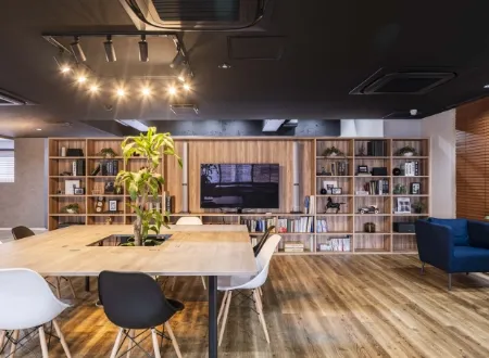木目調の書棚と大きなテーブルがある、落ち着いた雰囲気のモダンなオフィス休憩スペース