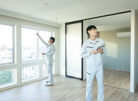 リフォーム中または点検中の室内で、タブレットを手に窓際を確認する作業服姿のスタッフ