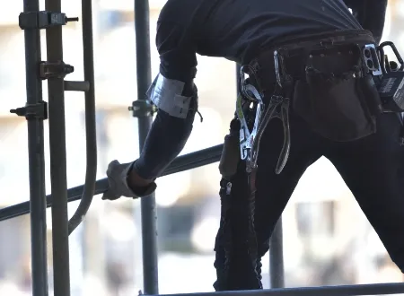 足場で作業を行う、腰道具を装着した建設現場の作業員の背面ショット