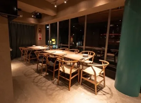木目調のテーブルとデザイナーズチェアが並ぶ、夜景が見えるおしゃれなレストランの店内