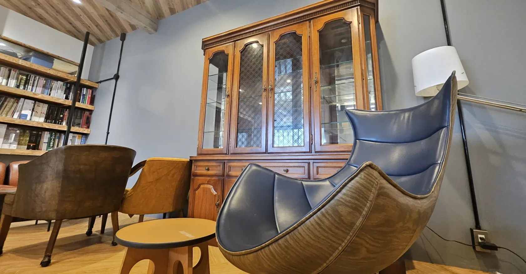 レトロな雰囲気の部屋。ユニークなデザインの青いレザーチェア、木製キャビネット、本棚、そして暖かい照明