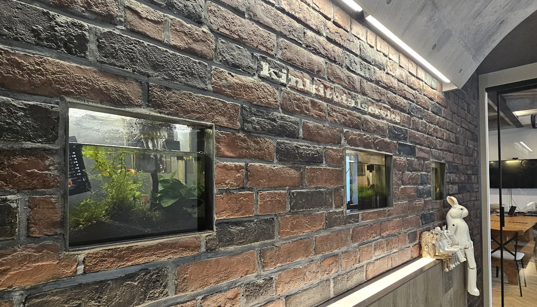 レンガ調の壁面に埋め込まれた水槽と会社ロゴ