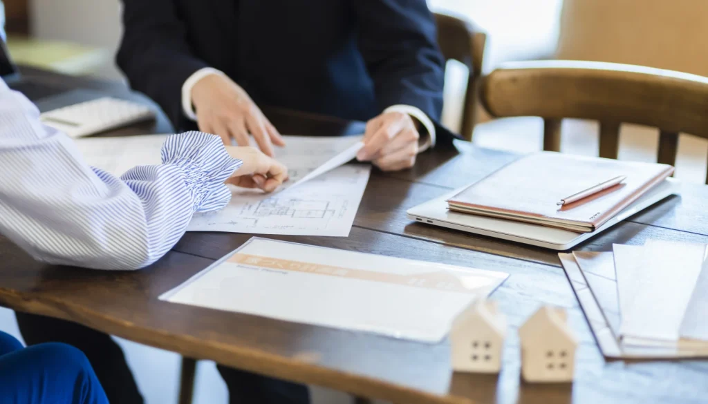 テーブルの上で住宅の間取り図を見ながら打ち合わせをする、担当者と顧客の手元の様子