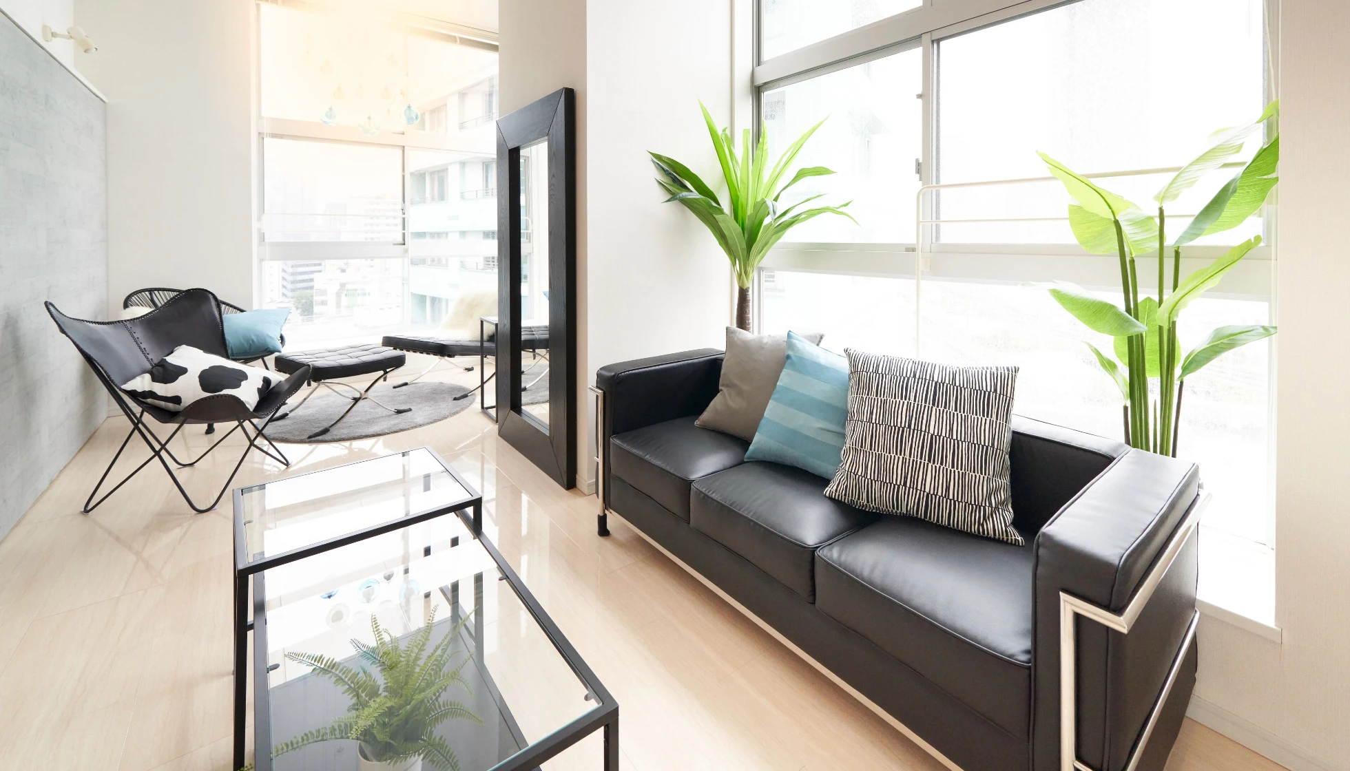 大きな窓から光が差し込む、黒のレザーソファとデザイナーズチェアを配置したモダンなリビングルーム